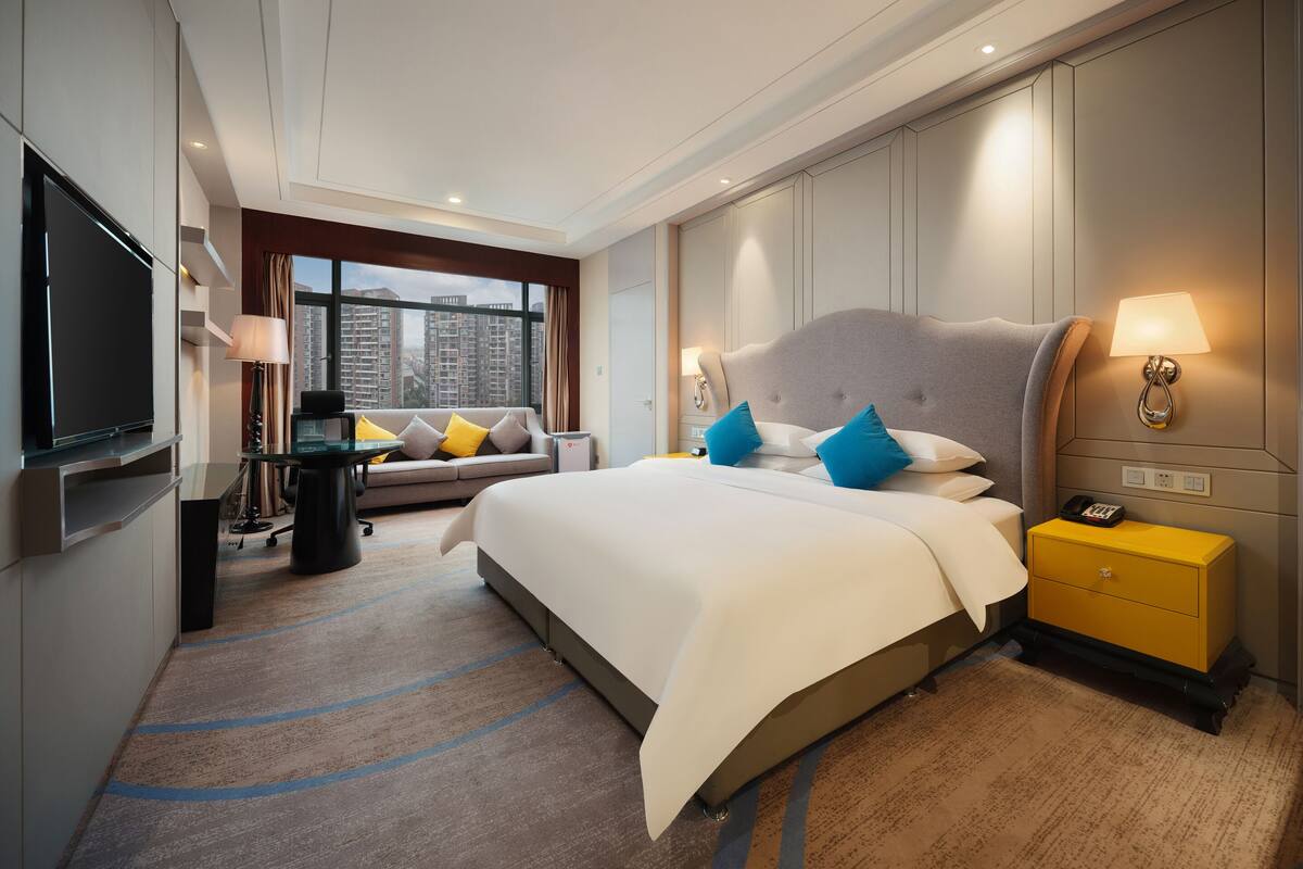 Une chambre d’hôtel moderne, dotée d’un grand lit, d’un canapé, d’une télévision et offrant une vue sur la ville.