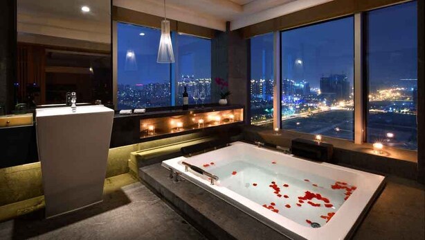 A modern bathroom with a large bathtub, a sink, and a mirror. It features large windows with a city view at night. - Chengdu Bvstin Boutique Hotel (Chengdu)