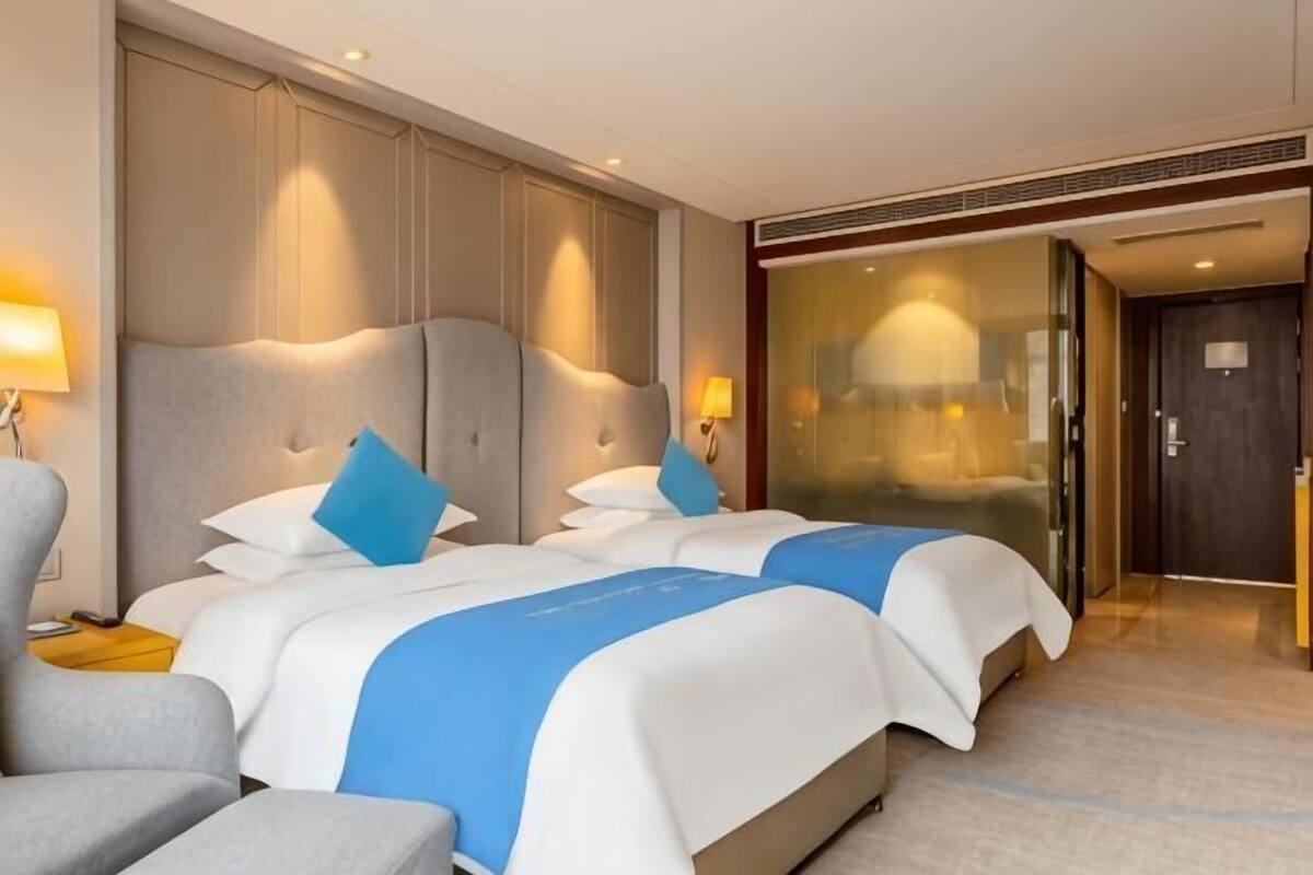 Une chambre d’hôtel avec deux lits, un canapé, un bureau et une cloison en verre.