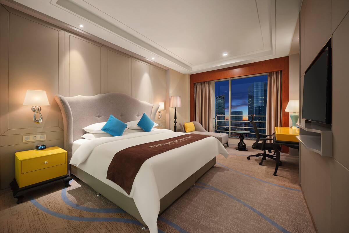 Une chambre d’hôtel avec un grand lit, des tables de chevet, un bureau, une chaise et un téléviseur.