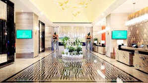 A modern hotel lobby with a geometric patterned floor, a central floral arrangement, and two digital screens displaying information. - Chengdu Bvstin Boutique Hotel (Chengdu)