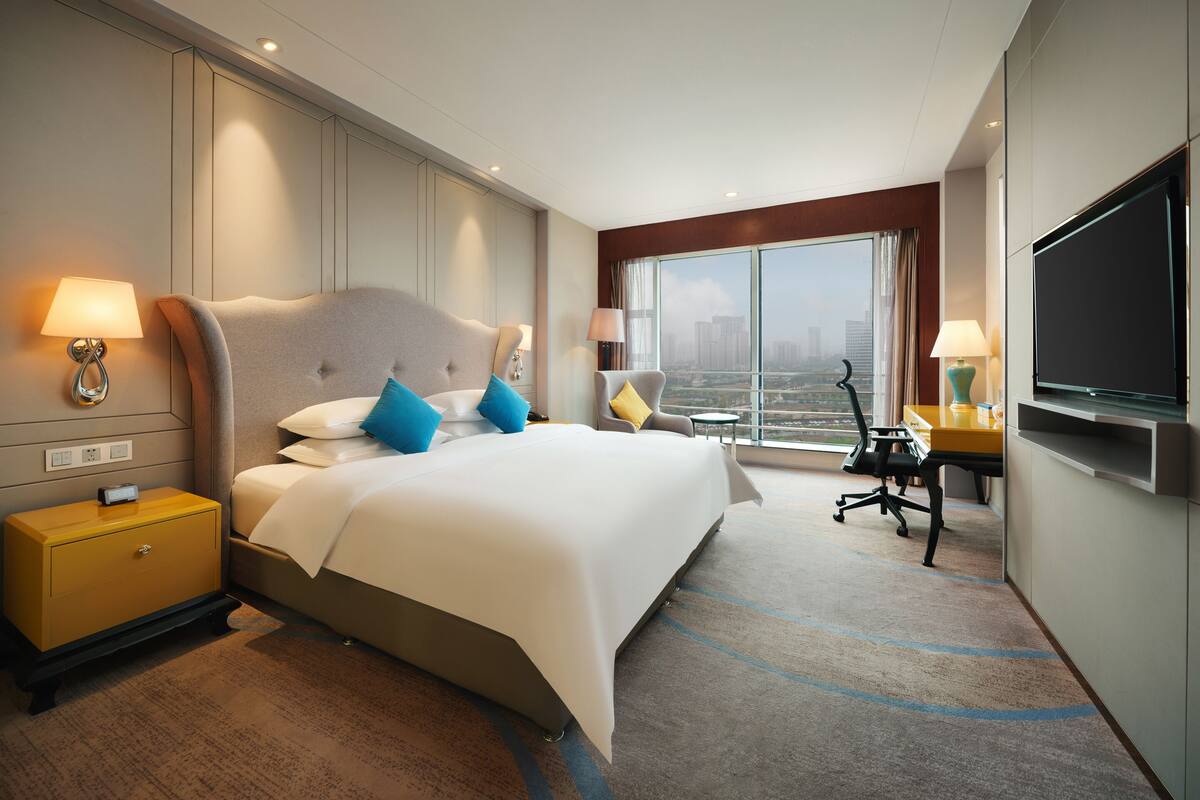 Une chambre d’hôtel avec un grand lit, des lampes de chevet, un bureau avec une chaise, une télévision et une vue sur la ville.