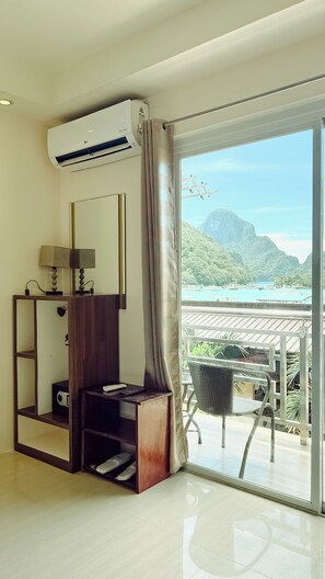 A modern room with a wooden desk, a lamp, and an air conditioning unit. A large window offers a view of a mountainous landscape and a pool. - MilanGrace Inn El Nido, Palawan (El Nido)