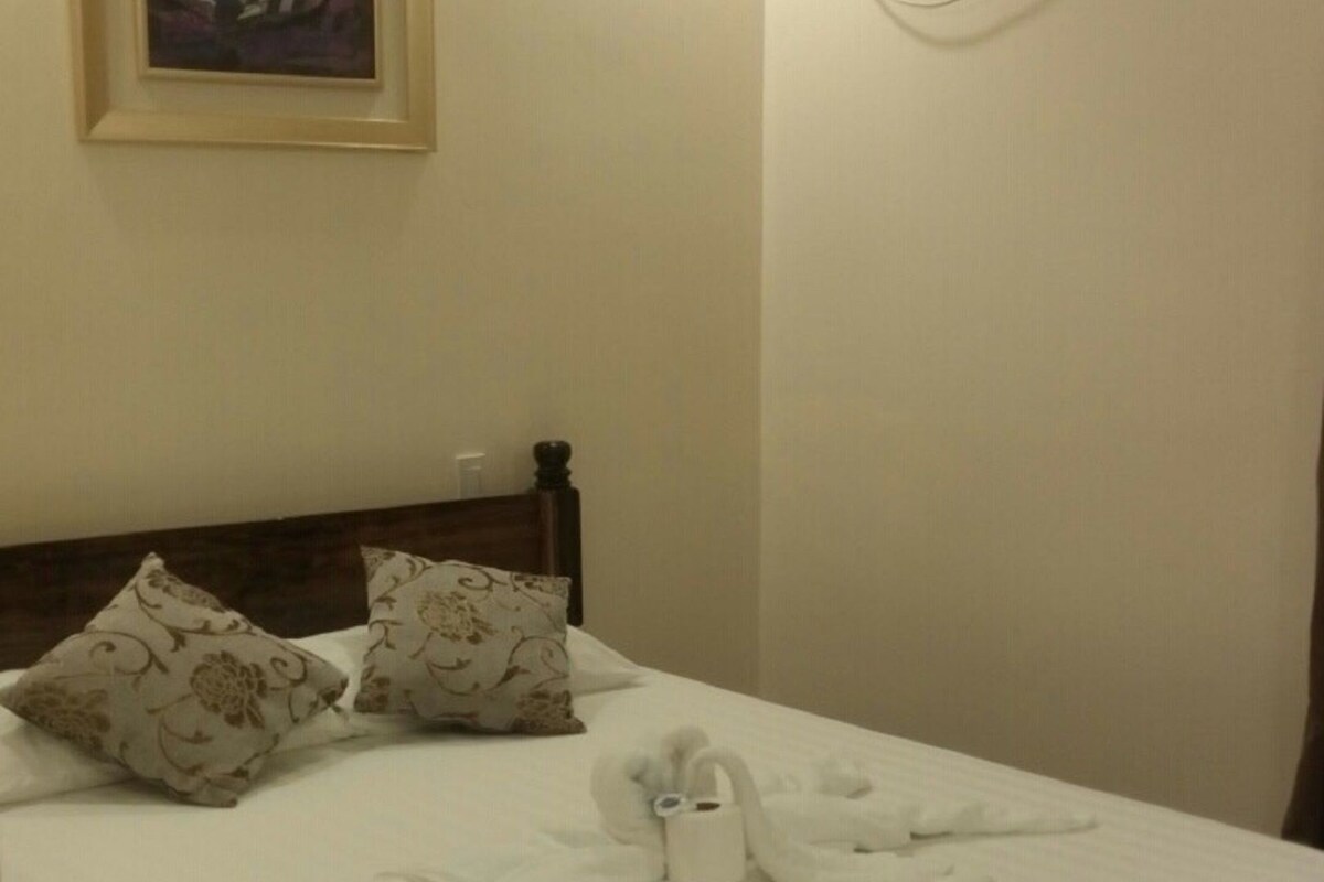 A neatly made bed with pillows, a framed picture on the wall, and an air conditioning unit.