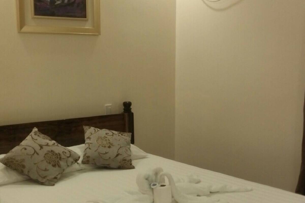 A neatly made bed with pillows, a framed picture on the wall, and an air conditioning unit.