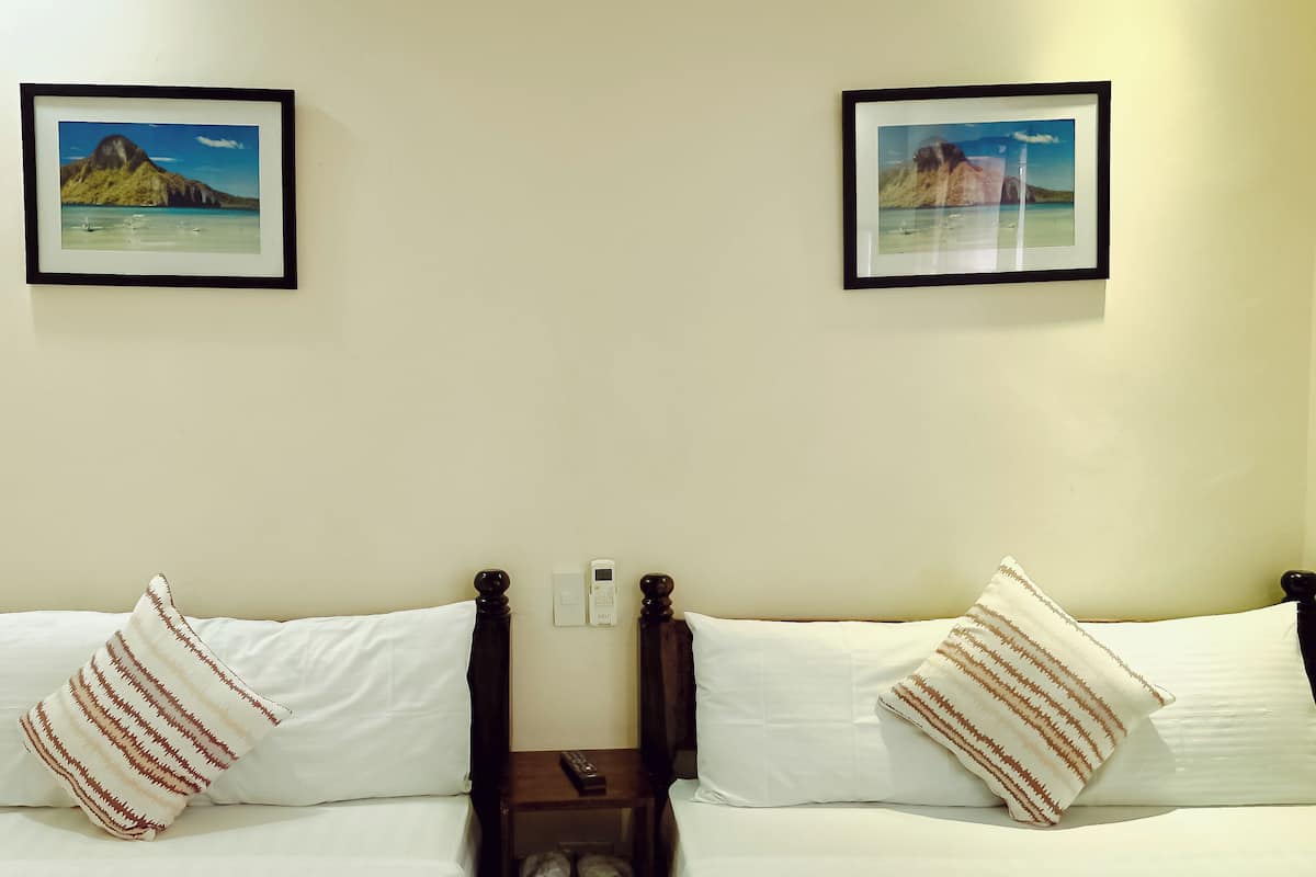 A double bed with white bedding and striped pillows, a nightstand with a remote control, and two framed pictures on the wall.