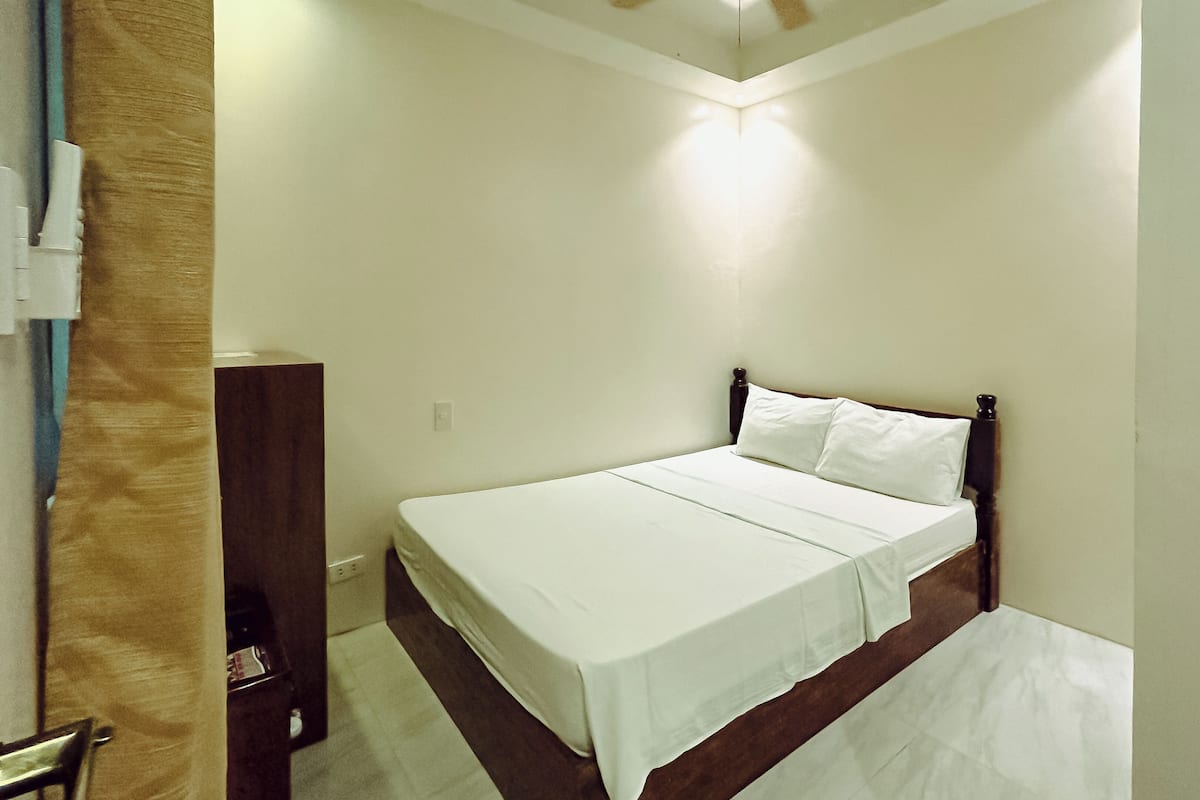 A small, neatly made bed in a room with white walls and a wooden headboard.