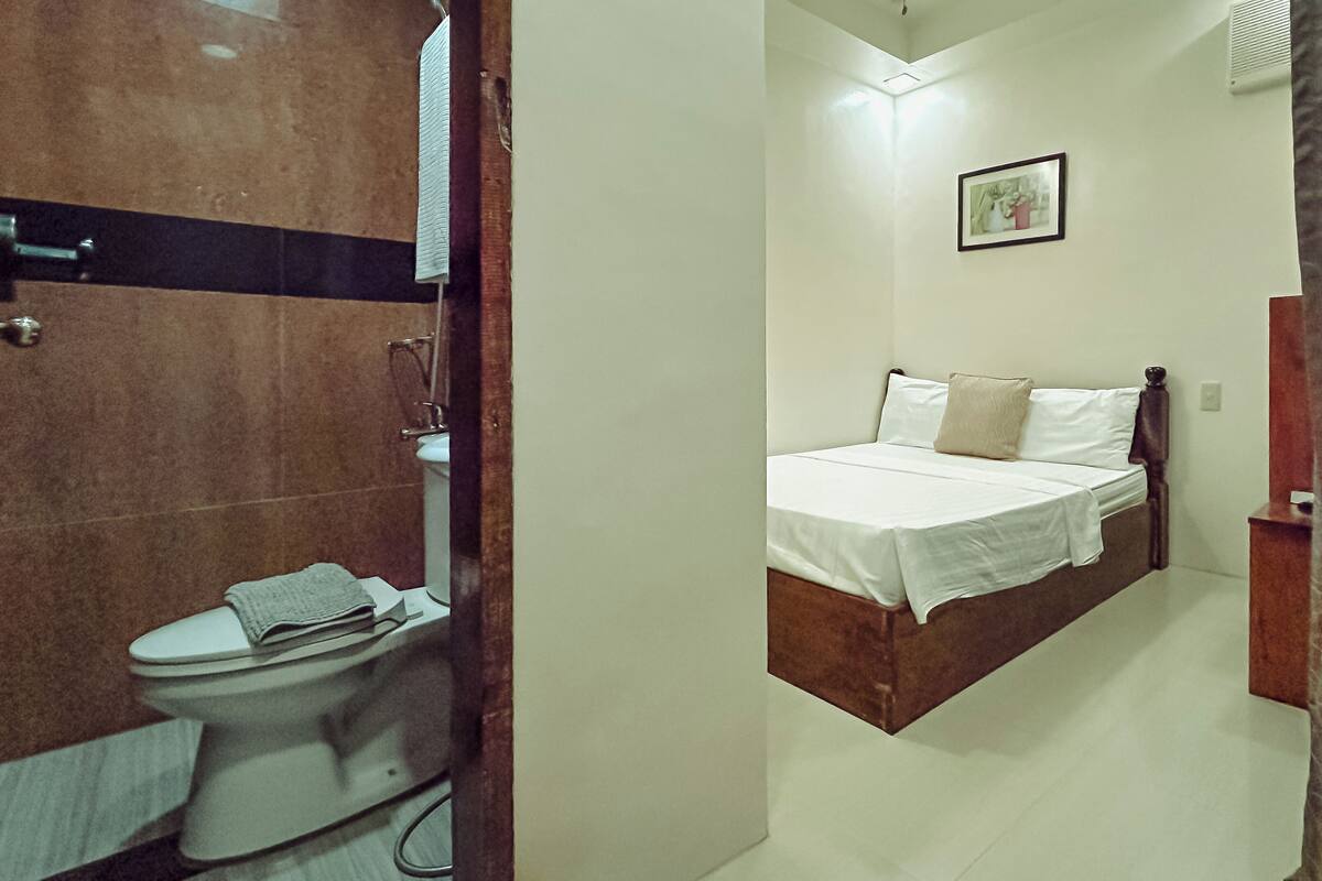 A bedroom with a bed, a bedside table, a toilet, and a shower area.
