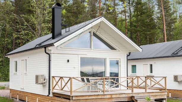 Une cabane blanche avec une terrasse en bois, de grandes fenêtres et une cheminée.