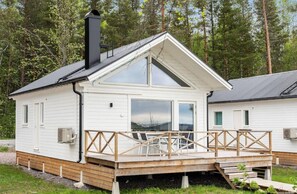A white cabin with a wooden deck, large windows, and a chimney.