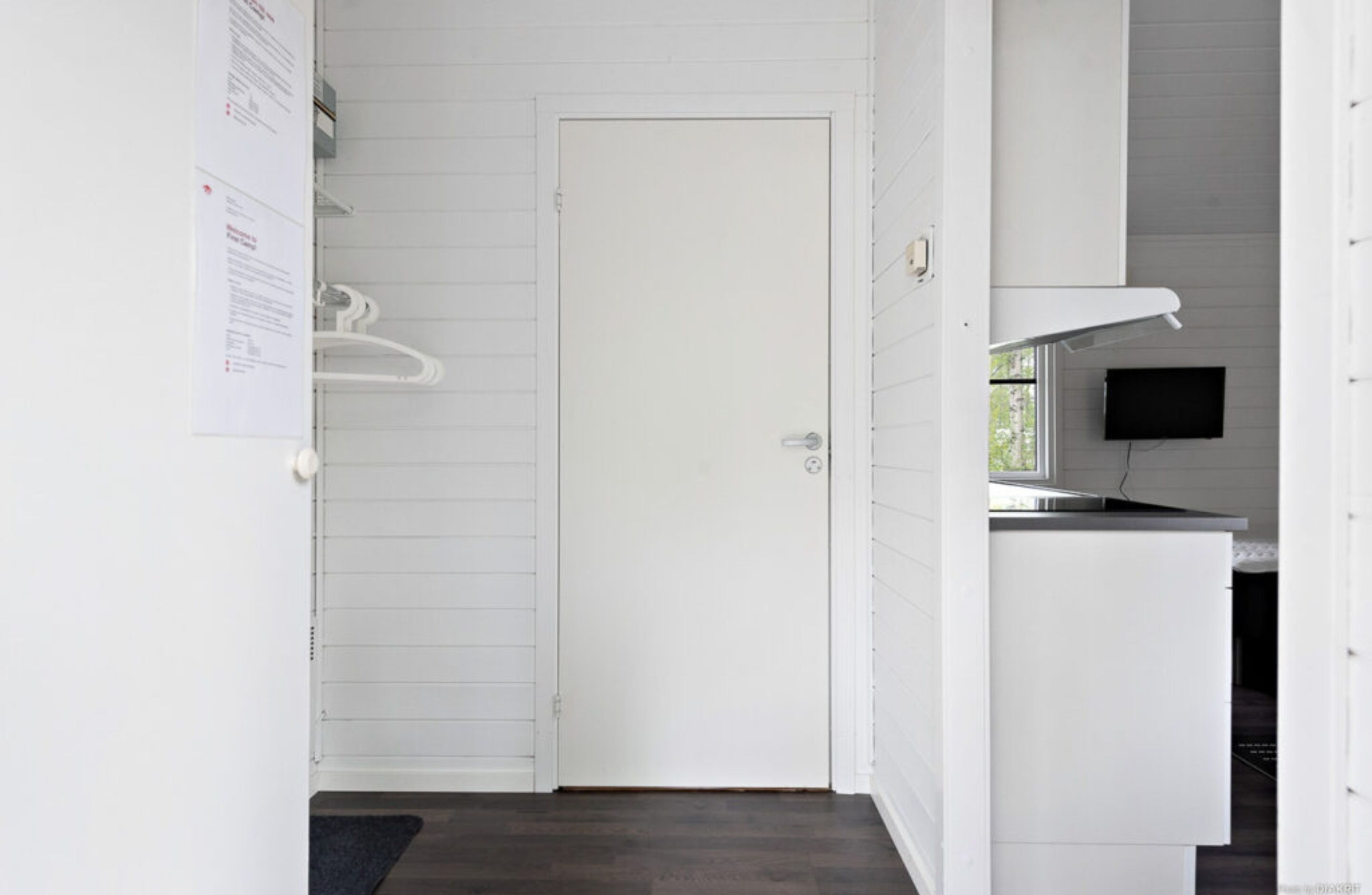 A clean, white interior with a closed door, a small kitchenette with a microwave, and a flat-screen TV mounted on the wall.