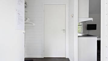 A clean, white interior with a closed door, a small kitchenette with a microwave, and a flat-screen TV mounted on the wall.