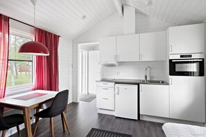 A modern kitchen with white cabinetry, a built-in oven, and a dining area with a table and chairs.