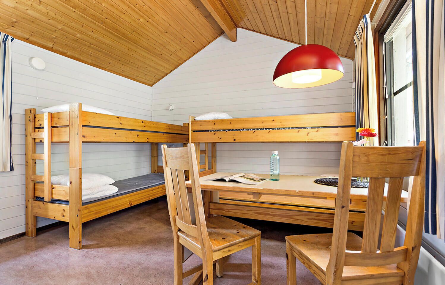A bunk bed room with a wooden desk, chairs, and a red pendant light.