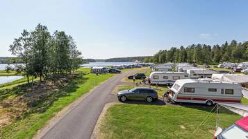 A campsite with RVs and cars parked along a road, surrounded by trees and a lake.