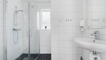 Un baño moderno con ducha de vidrio, un lavamanos blanco y un ventanal con una planta.