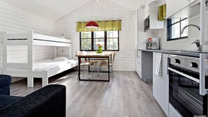 Une pièce compacte comprenant un lit superposé, une petite table à manger avec des chaises, un coin cuisine avec une cuisinière et une fenêtre avec des rideaux.