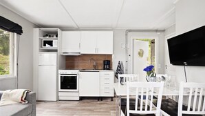 A compact kitchen with white cabinets, a microwave, a stove, and a coffee maker. There's a dining table with white chairs and a TV mounted on the wall.