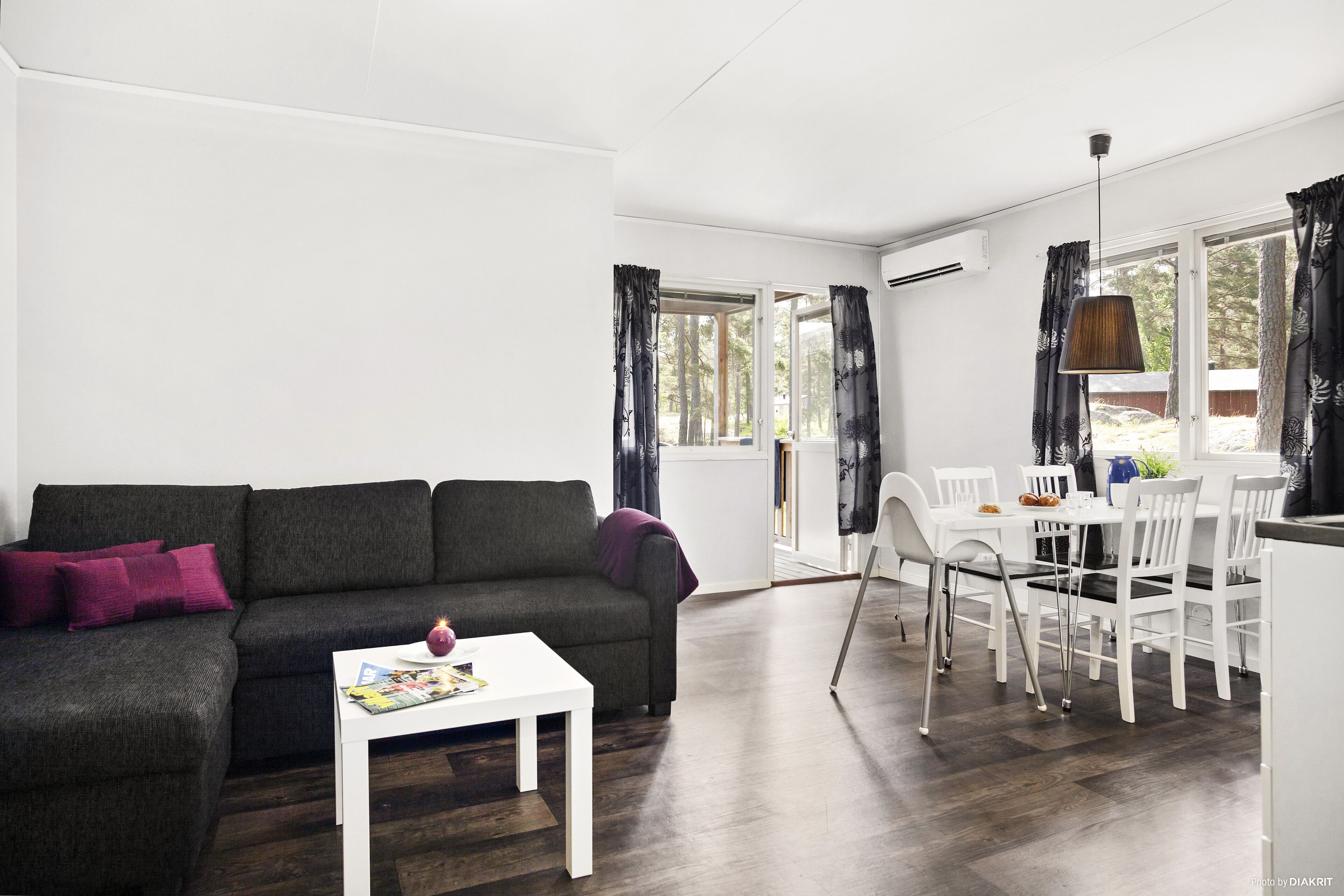 A modern living room with a dark grey sofa, white coffee table, and dining area with white chairs and a table.