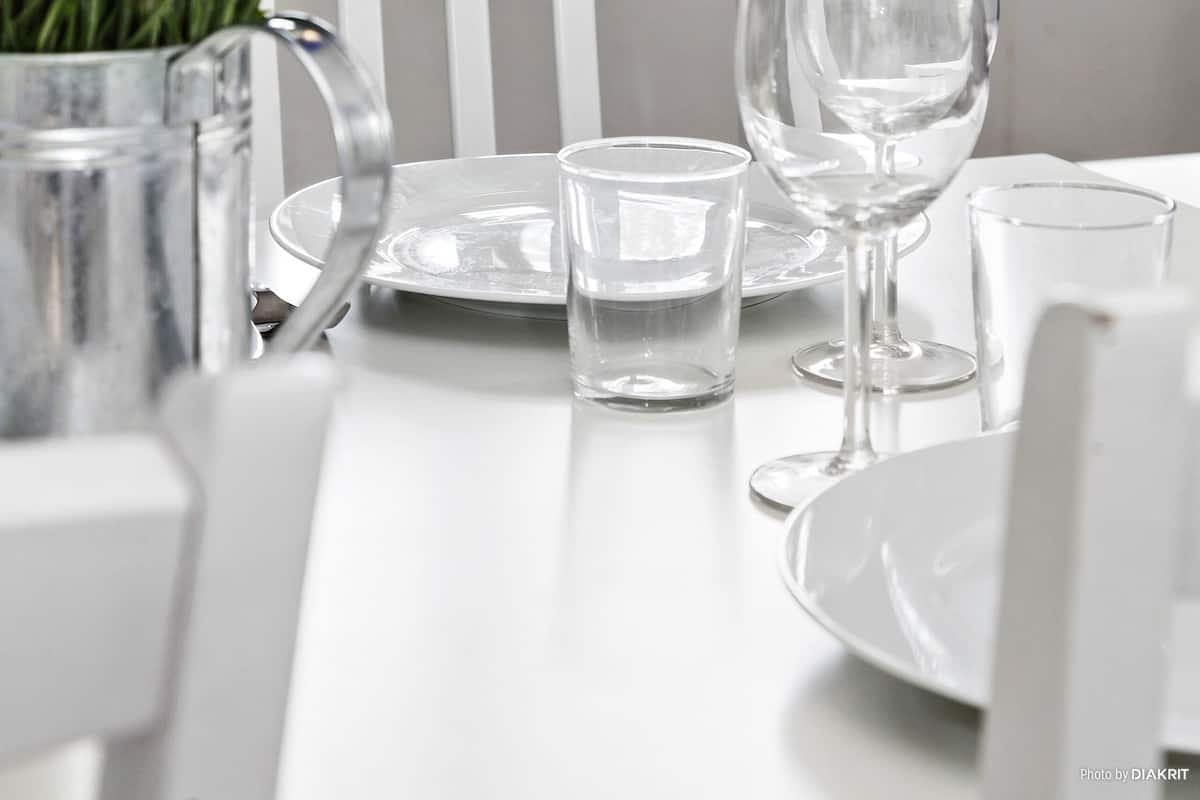 Una mesa de comedor con un florero de flores azules, una jarra y varios vasos y platos de vino.