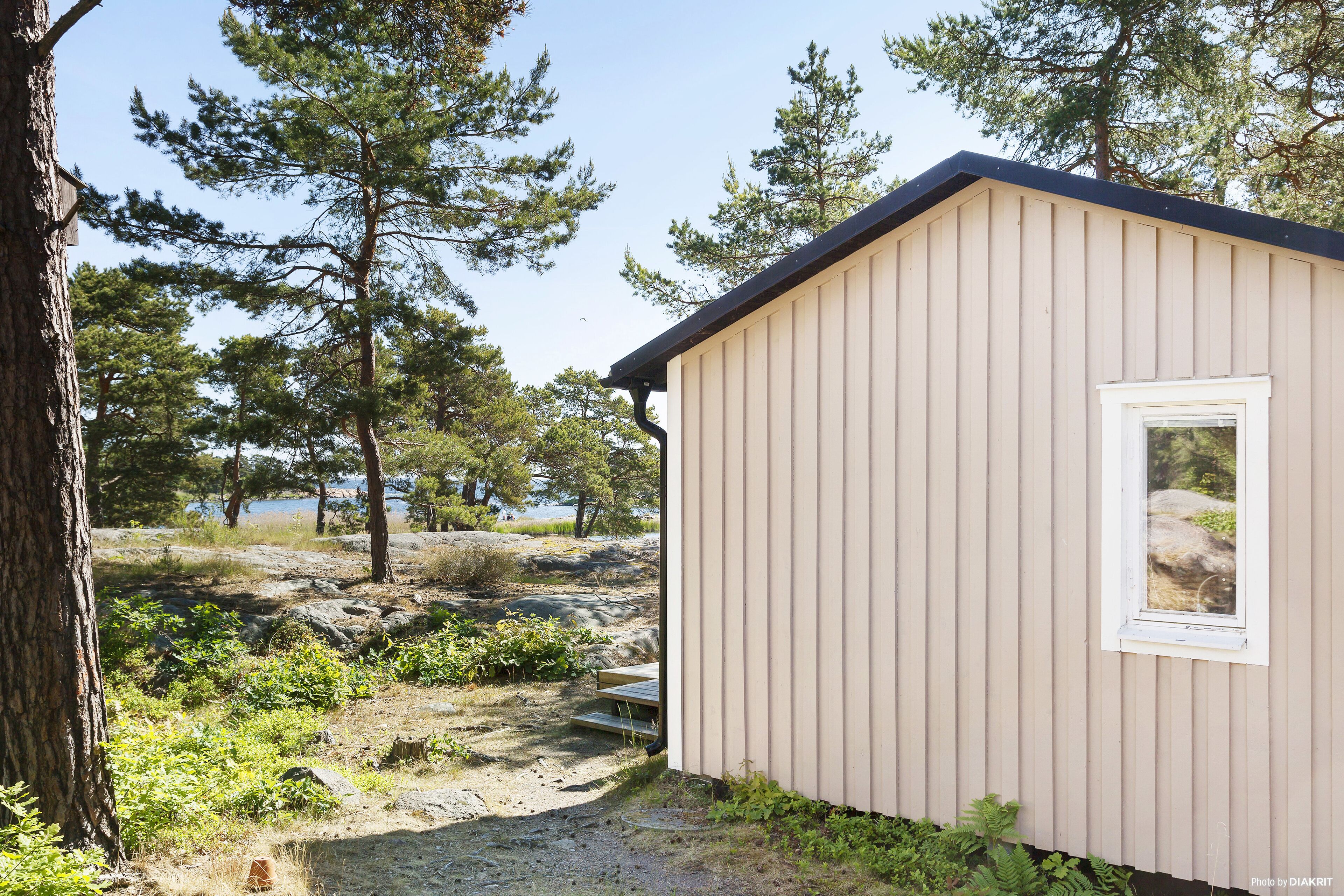 Un petit bâtiment d’un seul étage, à la façade beige et à la fenêtre blanche, entouré d’arbres et intégré dans un paysage naturel.