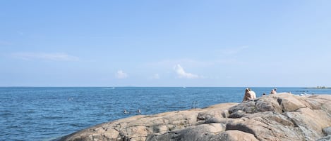 Un rivage rocheux bordé d’une eau d’un bleu limpide, où se trouvent quelques personnes.