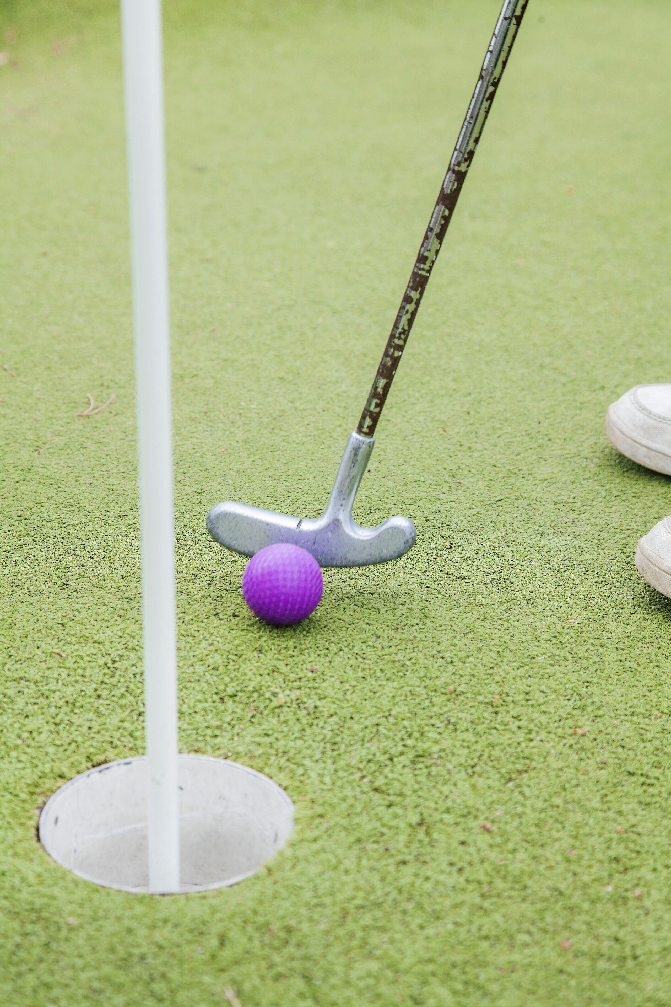 A golf ball near a hole with a putter on a green surface.