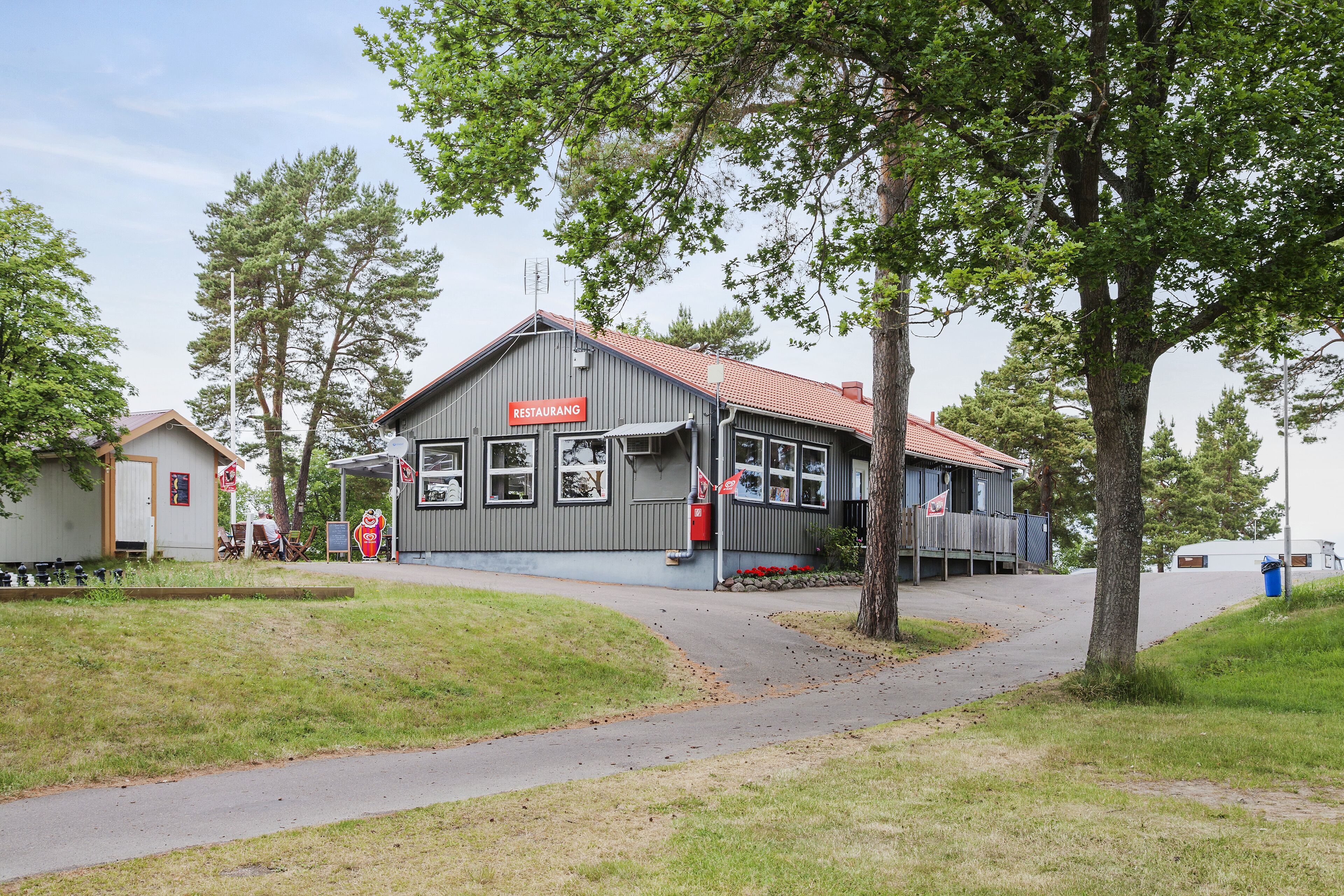 A restaurant with a red sign, a covered outdoor seating area, and a pathway leading to it.