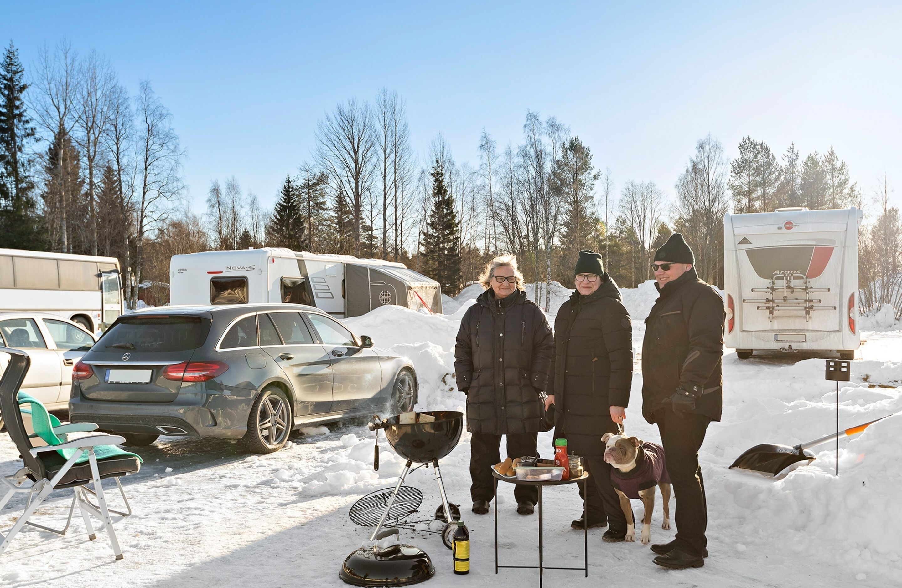 En gruppe mennesker står i et snækkedækket udendørsområde med autocampere og en bil parkeret i nærheden.