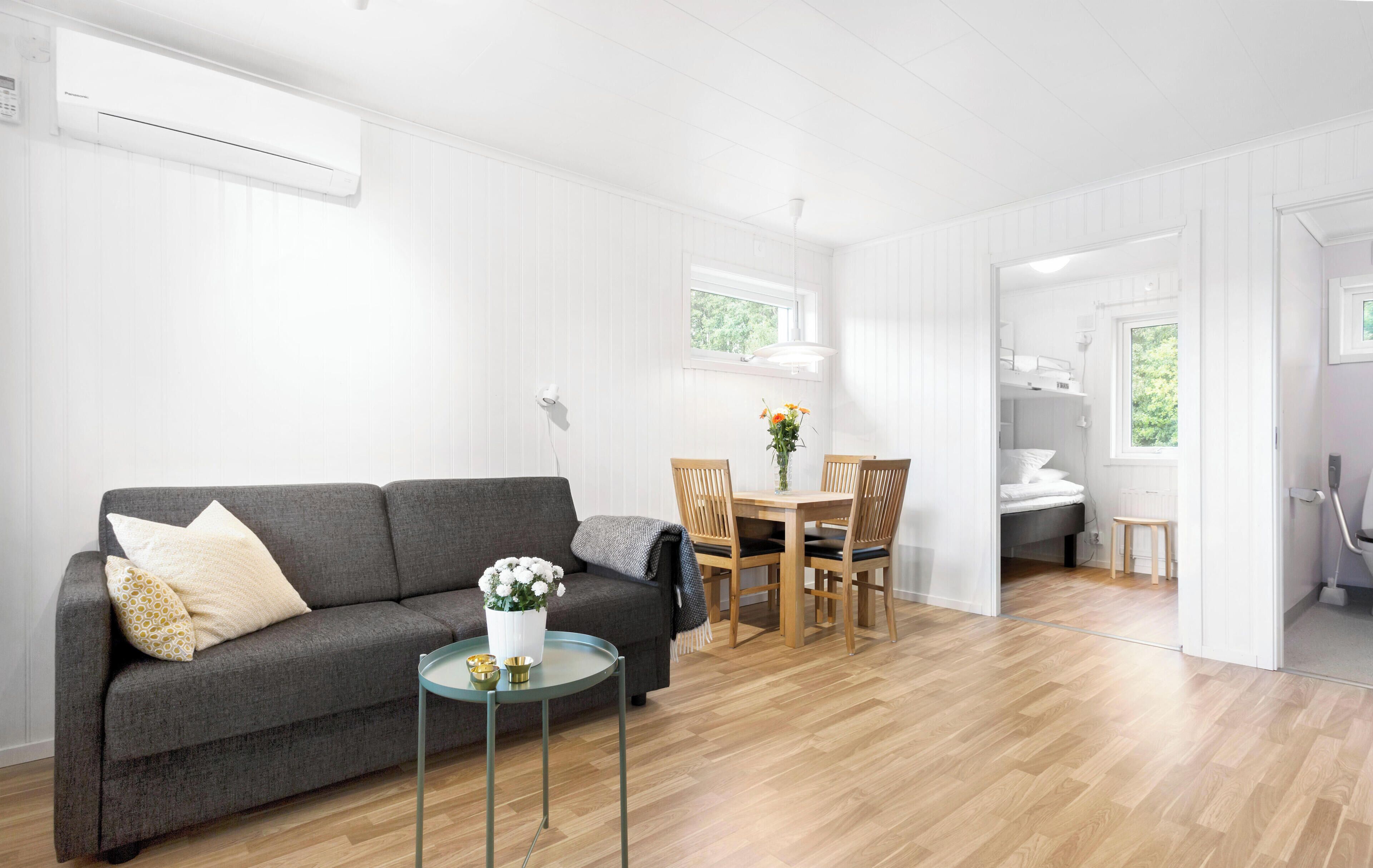 A modern living room with a grey sofa, a small round table, and a dining area with wooden chairs and a table.
