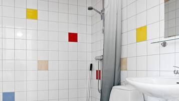 Ein Badezimmer mit weißen Fliesen, einer Dusche, einer Toilette und einem Waschbecken.