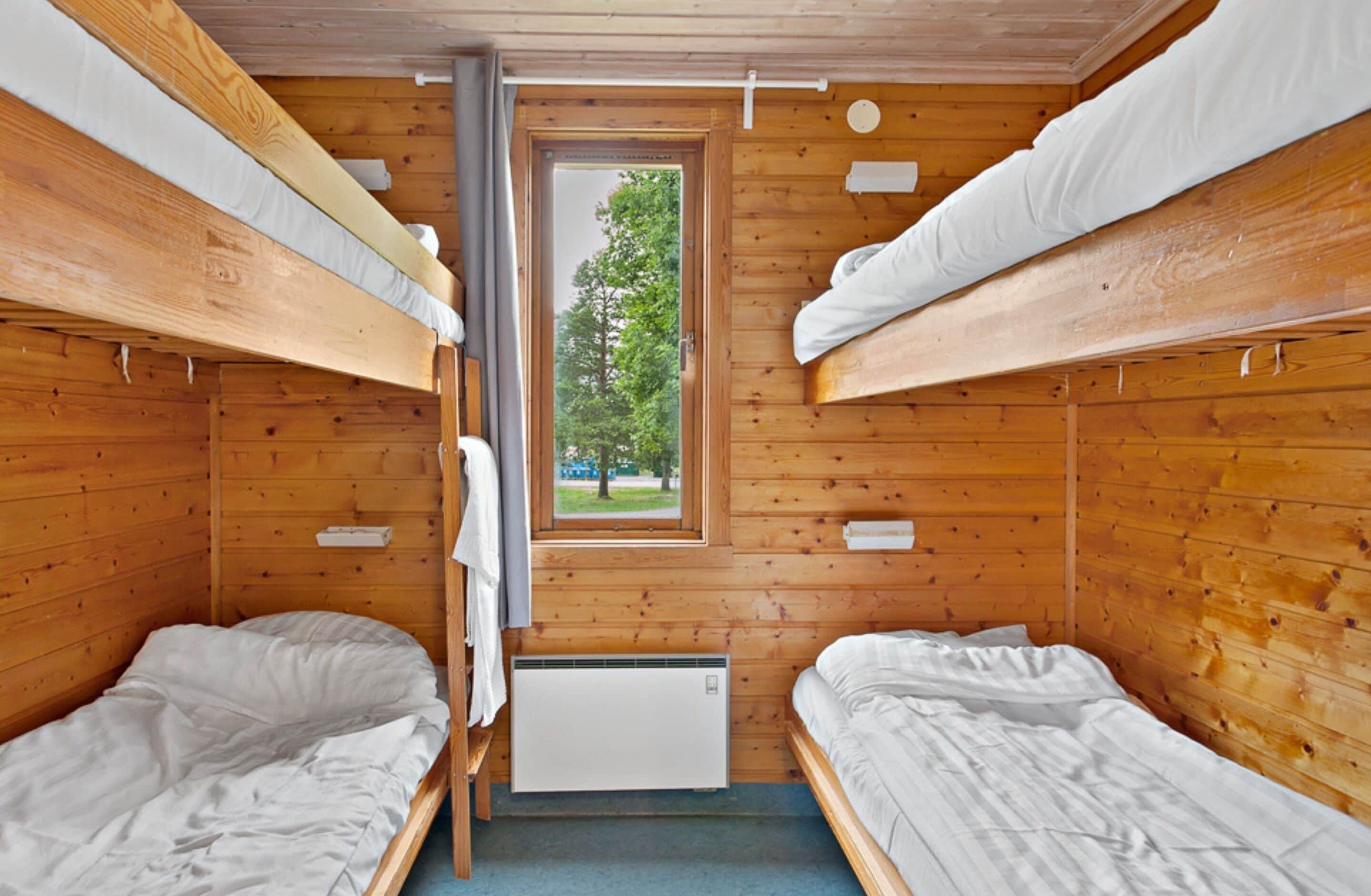A cabin with two bunk beds, a window with a view of trees, and a small heater.
