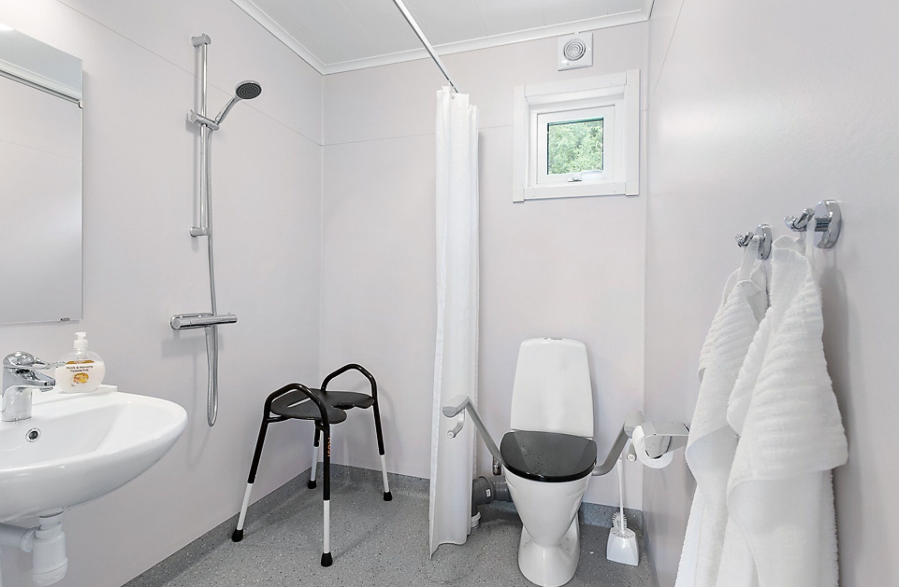 Un baño con lavamanos blanco, ducha, inodoro y una silla.