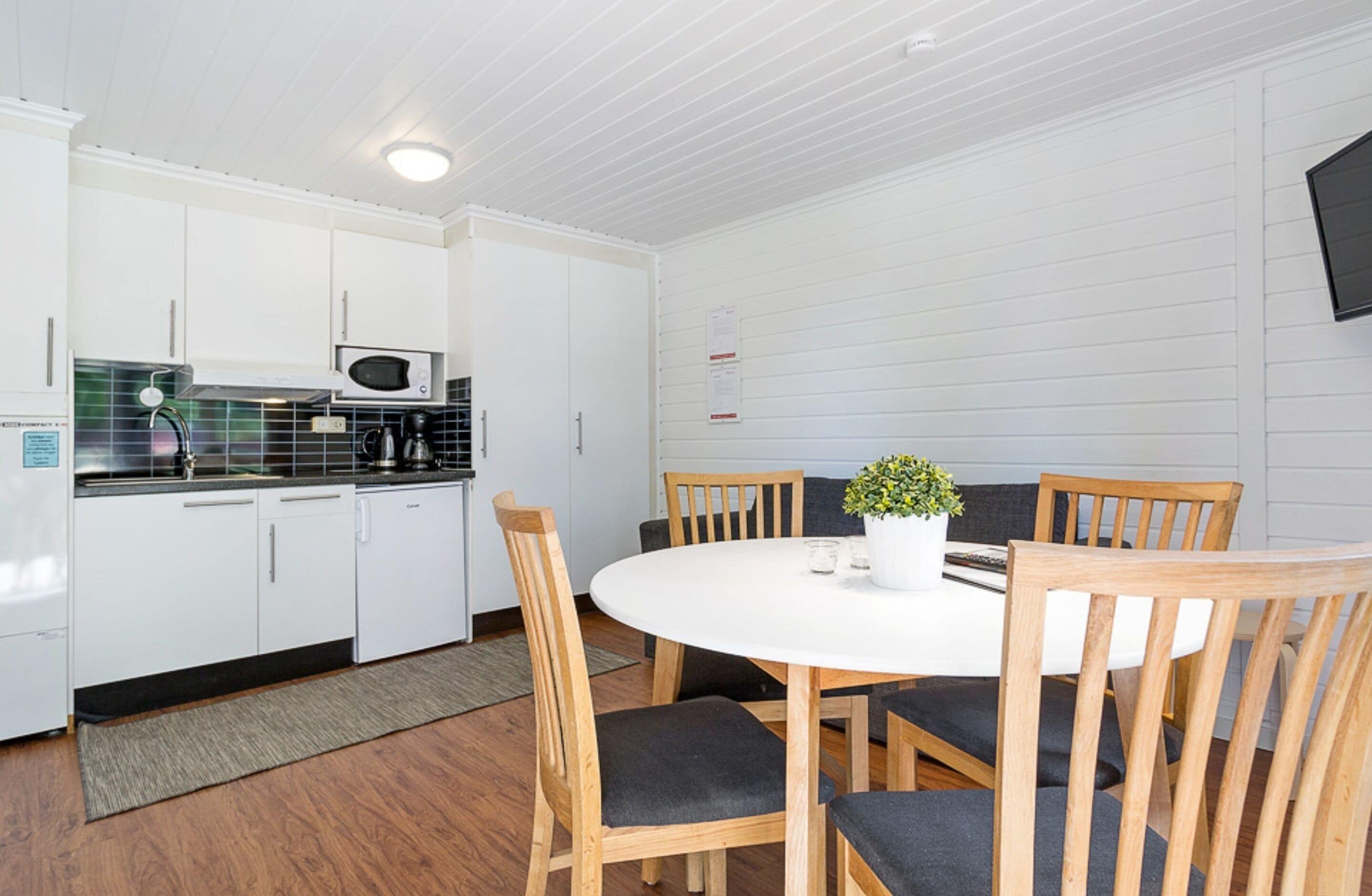 A compact kitchen with white cabinets, a microwave, and a dining area with a round table and wooden chairs.