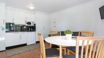 A compact kitchen with white cabinets, a microwave, and a dining area with a round table and wooden chairs.
