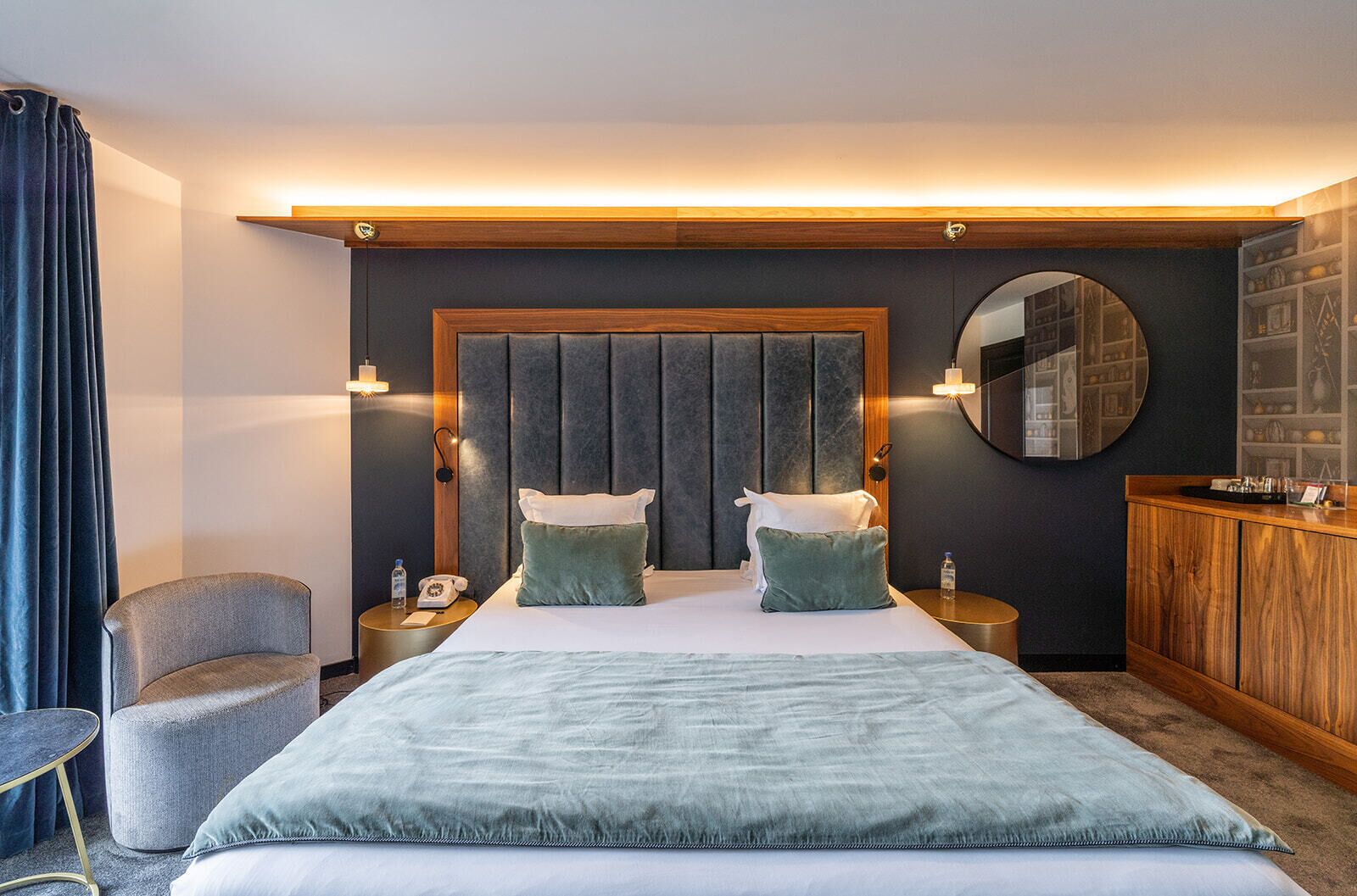A hotel room with a large bed, a round mirror, a wooden cabinet, and a chair.