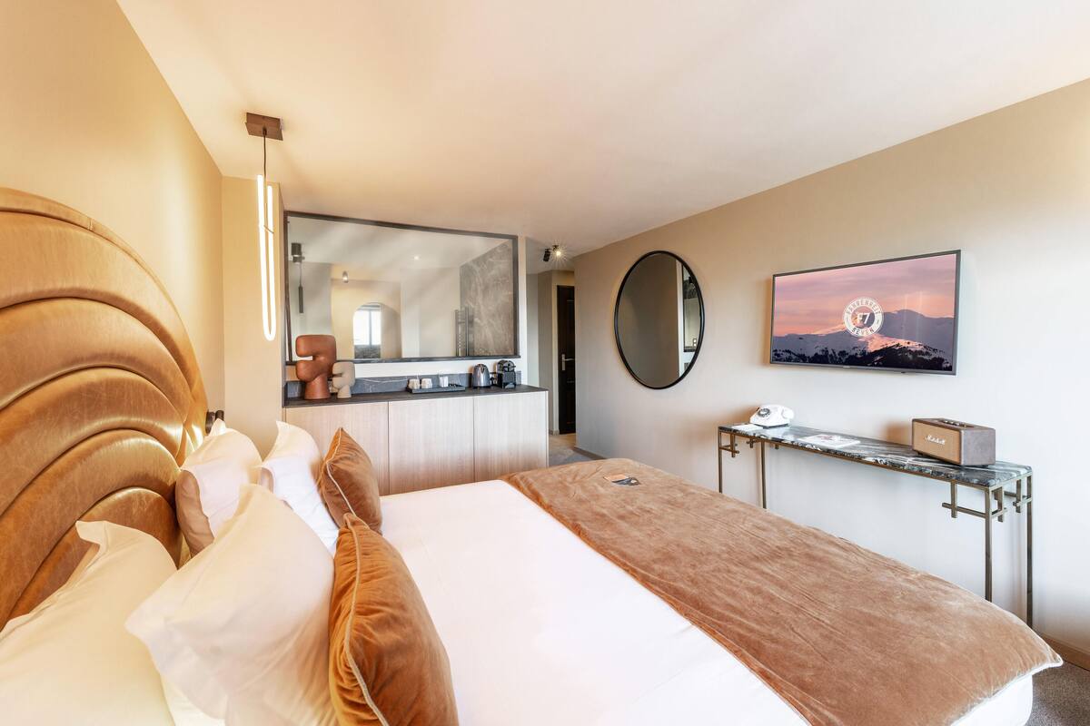 A modern hotel room with a large bed, a bedside table, a mirror, and a view of the bathroom.