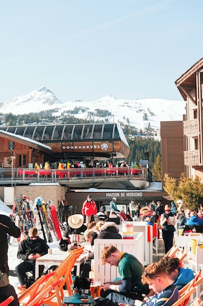 Ein Skigebiet mit einem Holzbäude, im Hintergrund sind 'COURCHEVEL' und 'MAISON DE MORIAND' zu sehen.