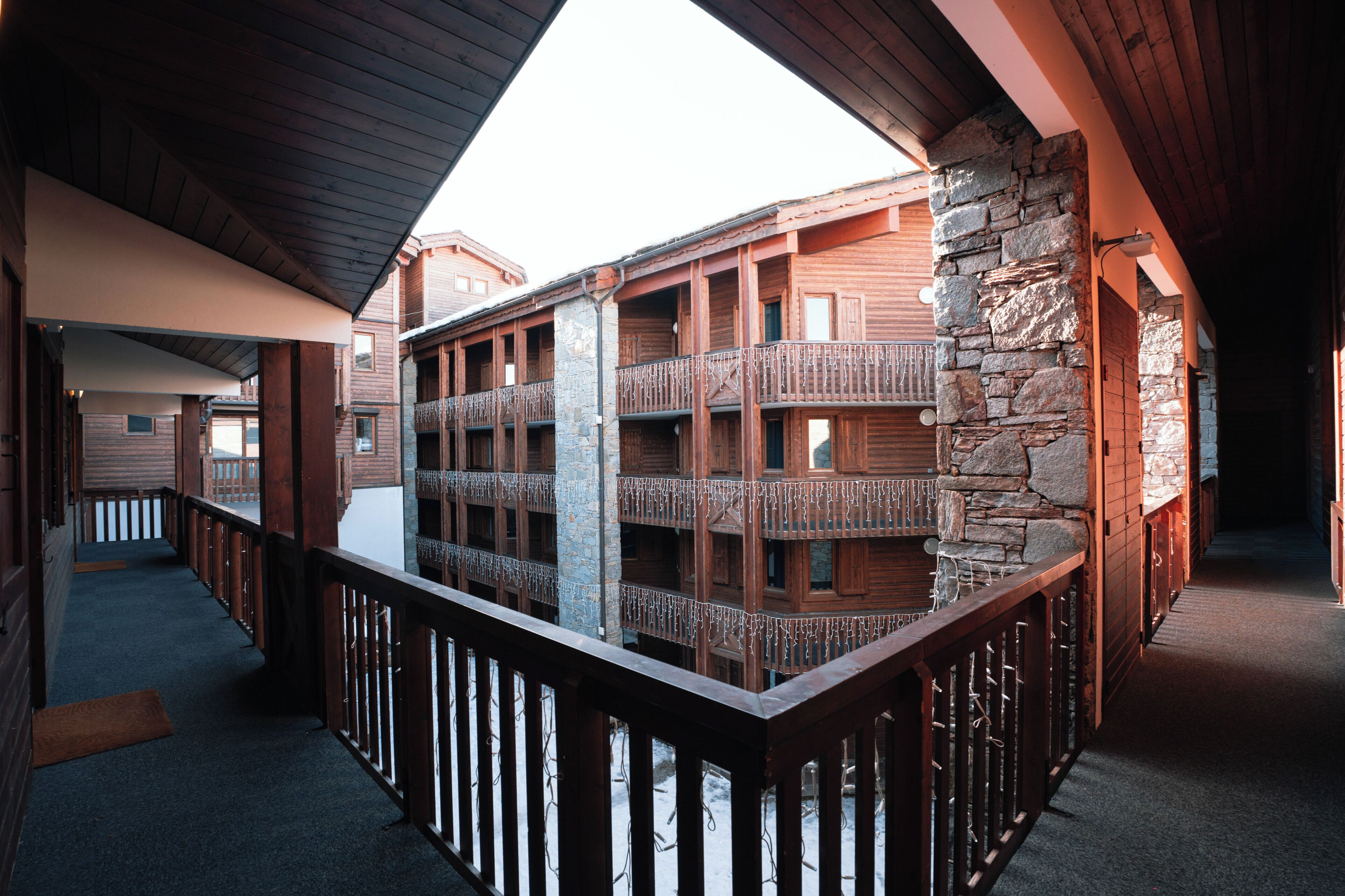 A wooden building with balconies, a stone wall, and a wooden railing.