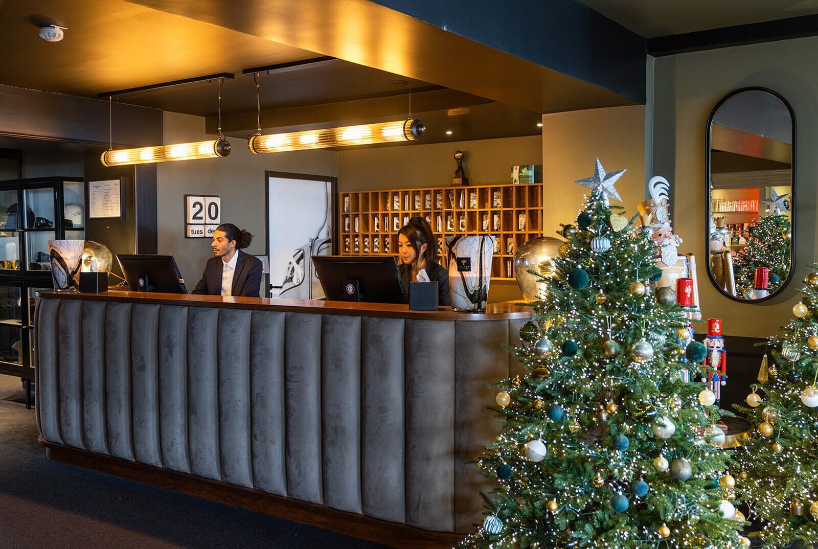A reception desk with two employees, a Christmas tree, and a mirror.