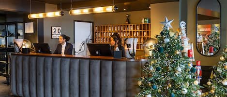 A reception desk with two employees, a Christmas tree, and a mirror.