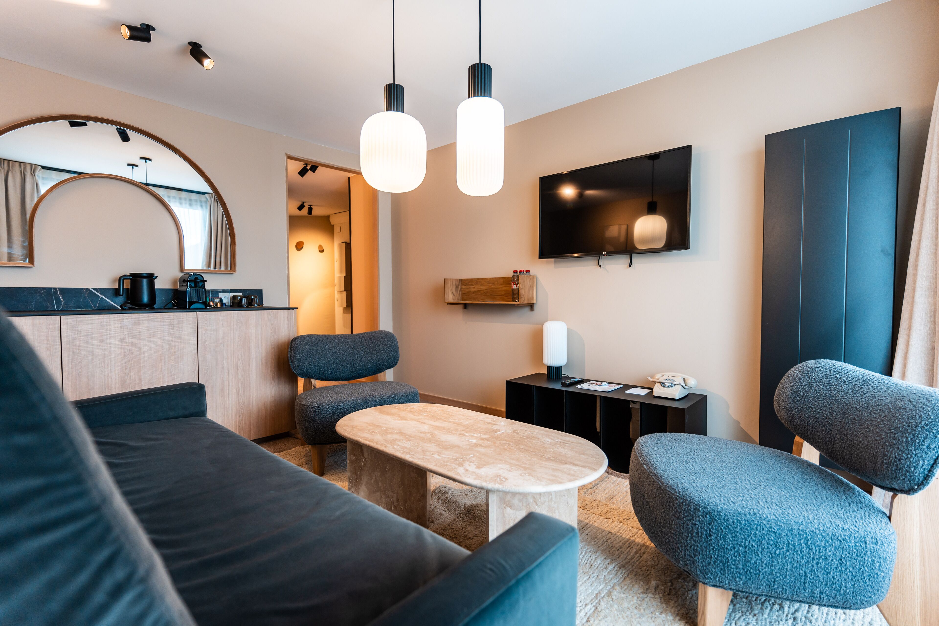 Un salon moderne comprenant un canapé, deux fauteuils, une table basse et un téléviseur fixé au mur.