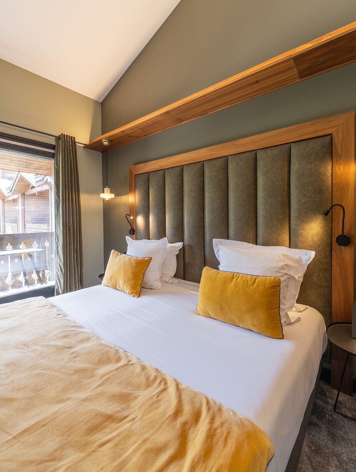 A hotel room with a large bed, wooden headboard, two bedside lamps, and a view of a balcony.