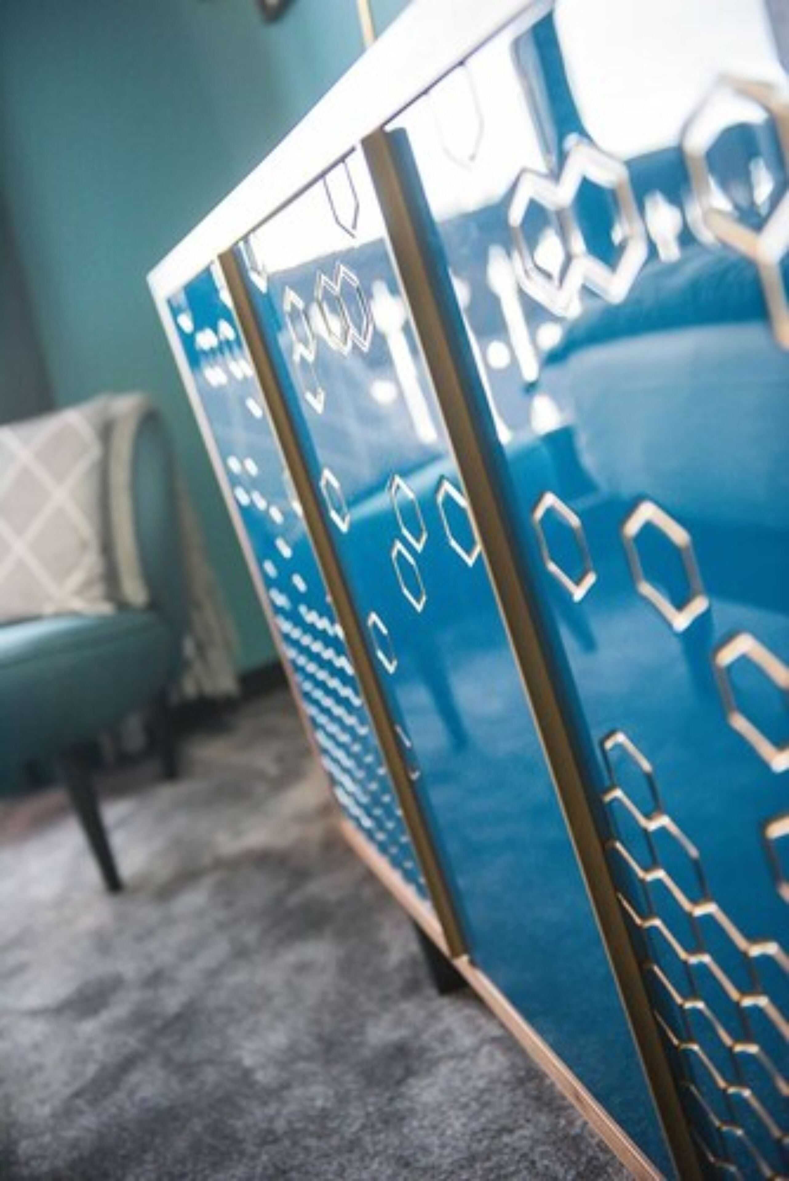 A room with a teal sofa, a patterned rug, and a blue cabinet with hexagonal designs.
