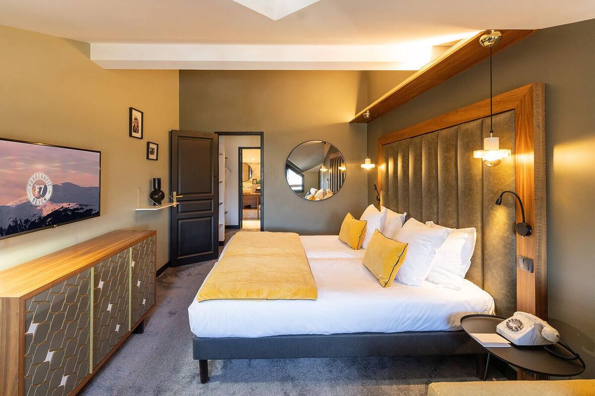 A hotel room with a large bed, a desk with a telephone, a TV, a mirror, and a wooden headboard.
