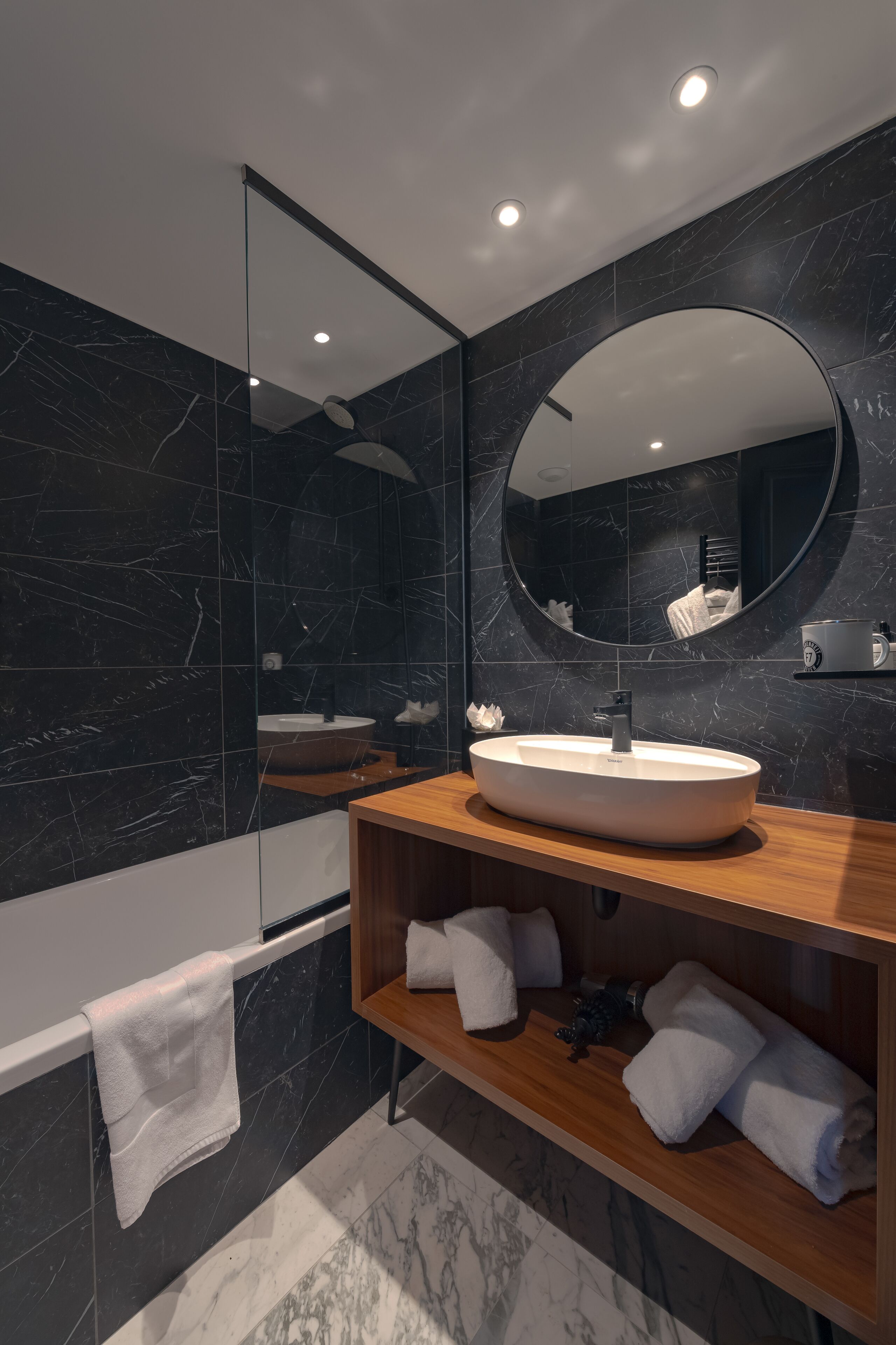 A modern bathroom with a large mirror, a round sink, and a wooden vanity.