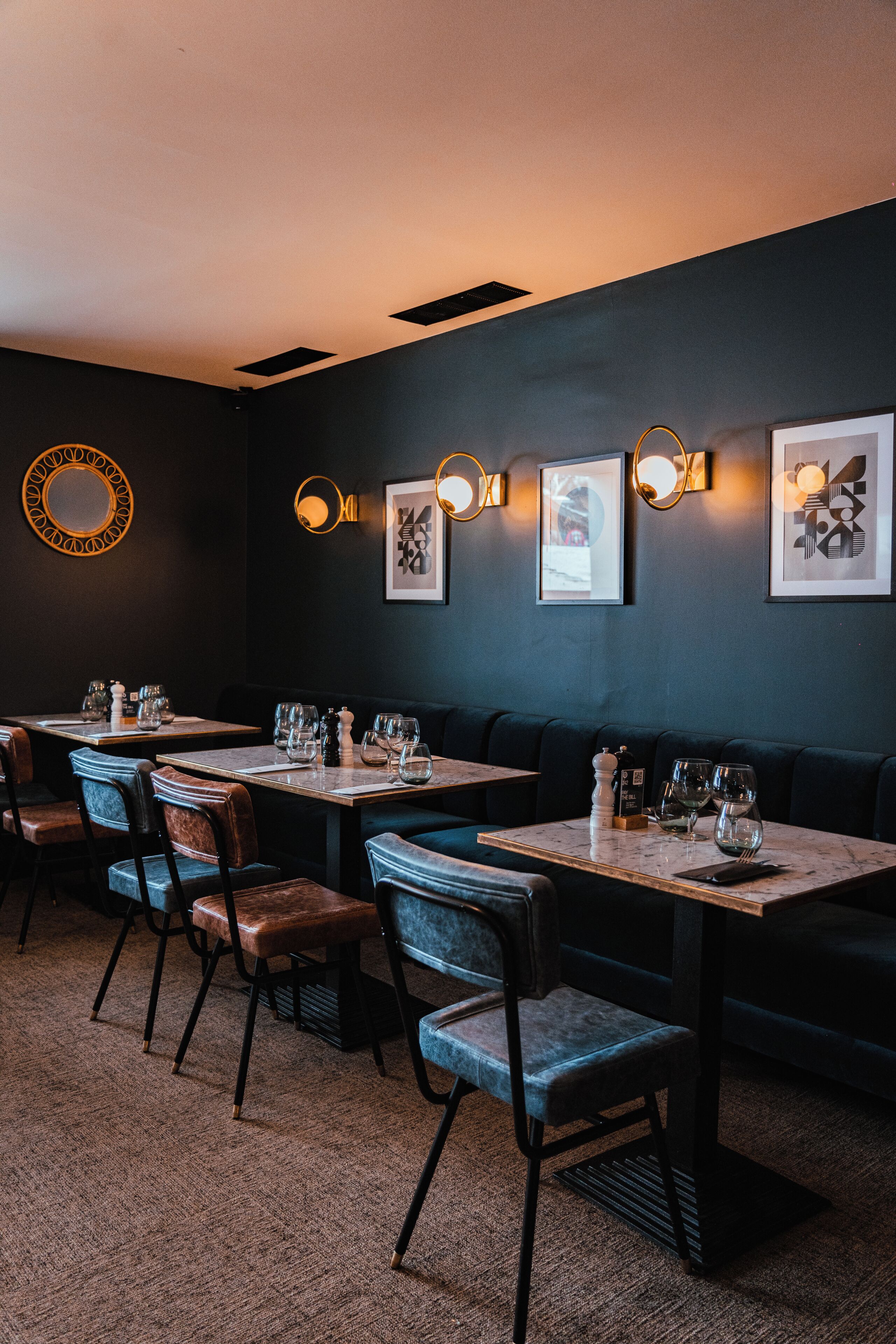 Un restaurante con paredes oscuras, mesas redondas y asientos acolchados.