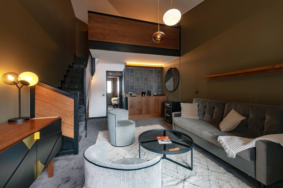 A modern living room with a sofa, coffee table, and armchair. A staircase leads to an upper level.