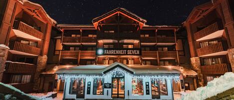 Un hotel con un letrero que dice 'FAHRENHEIT SEVEN', balcones y la entrada a un bar de esquí.