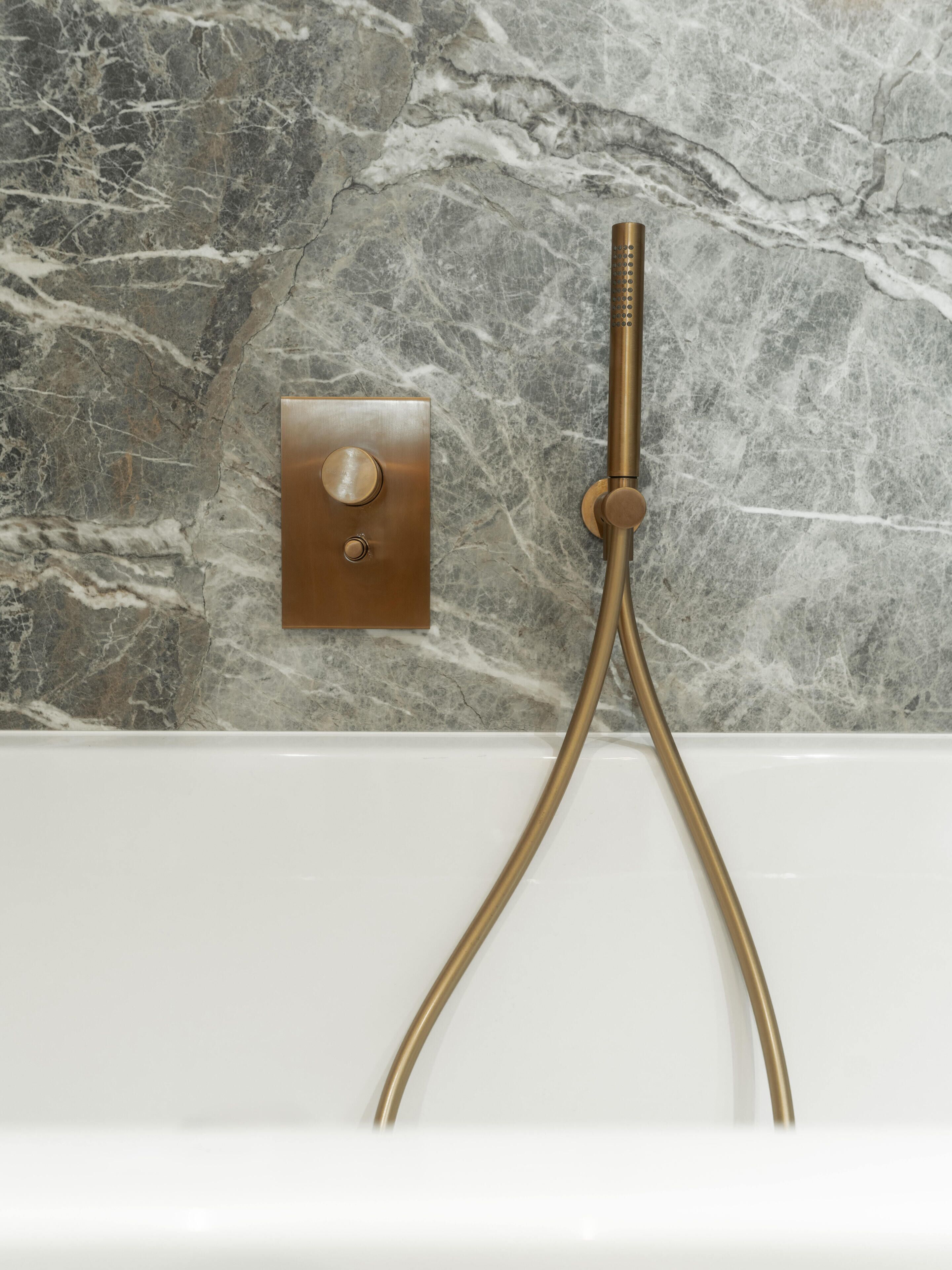 Bagno con parete in marmo, pannello comandi doccia dorato e soffione dorato.